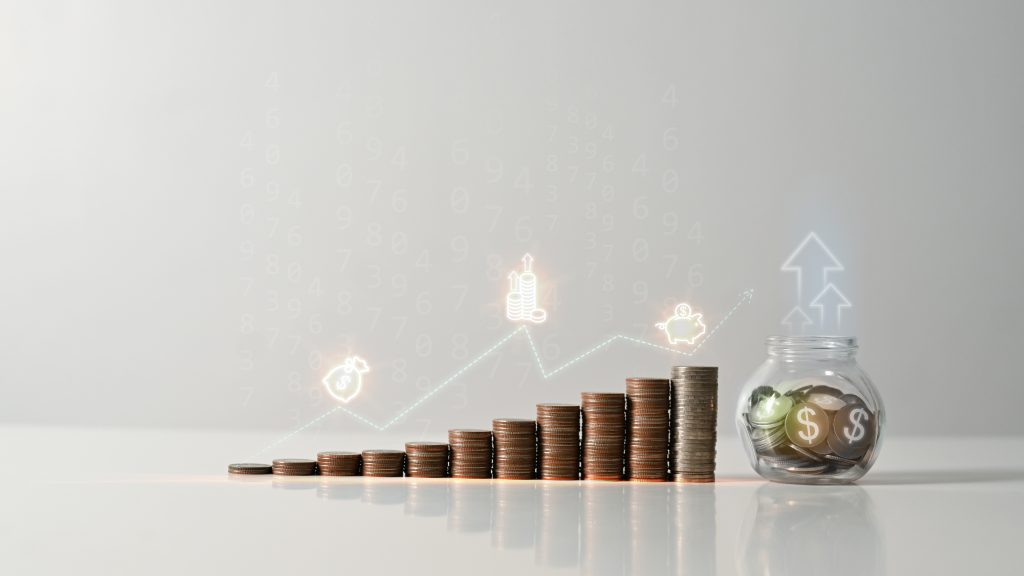 Graphique symbolisant la croissance financière avec des pièces de monnaie empilées et un pot en verre rempli de pièces et de billets, sur fond gris.